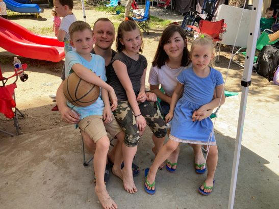 A family -- two parents and three kids -- gather for a photo at an encampment. One of the children holds a basketball. 