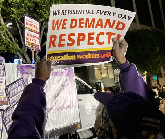 Someone holds up a sign at the rally; the sign says "We demand respect" in all caps